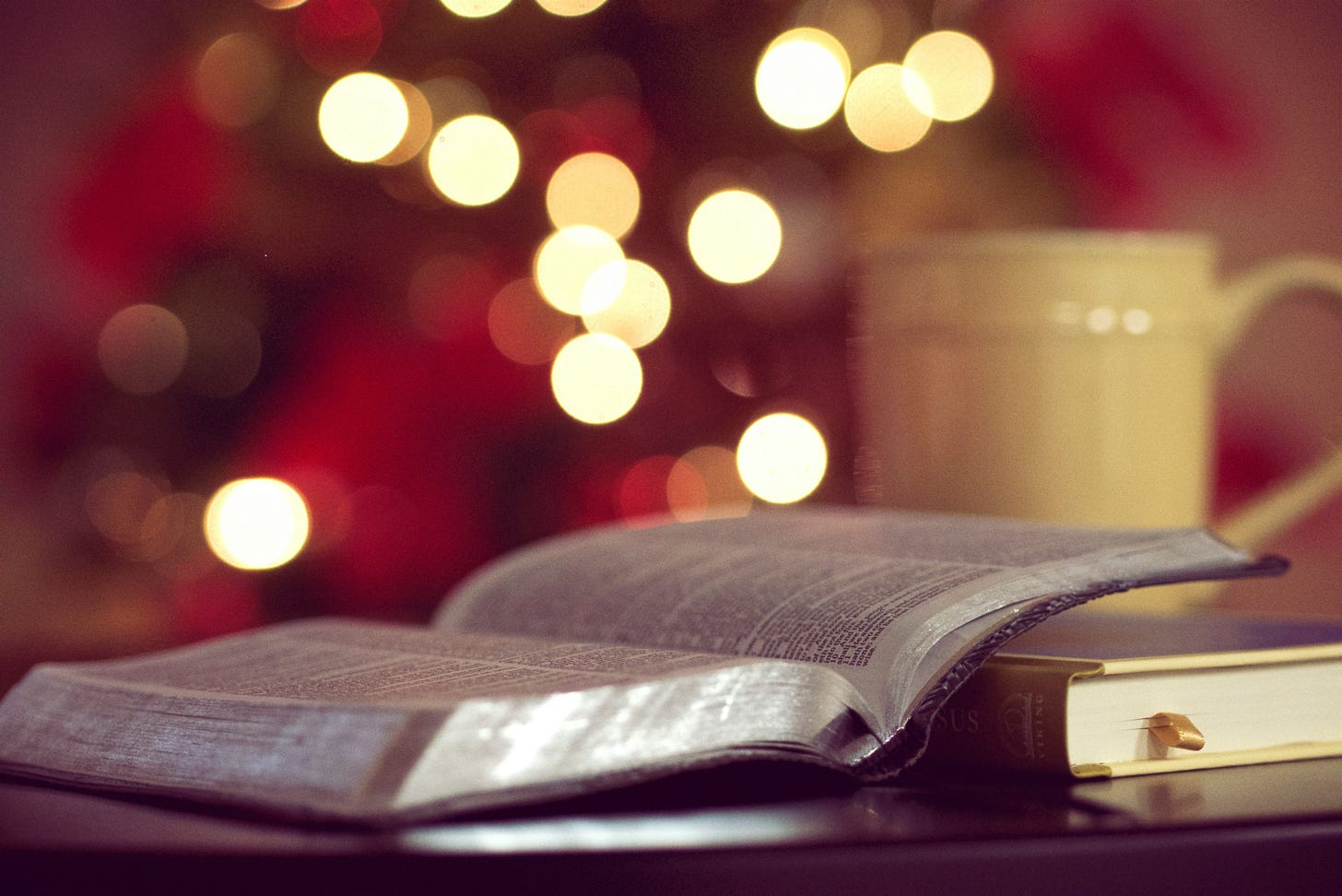 Image of Bible close up shot with coffee cup and lights in the background.