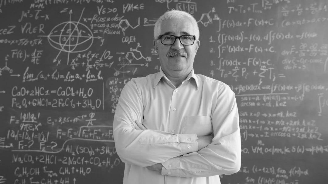 A smiling professor stands arms crossed by chalkboard A smiling professor stands arms crossed by chalkboard