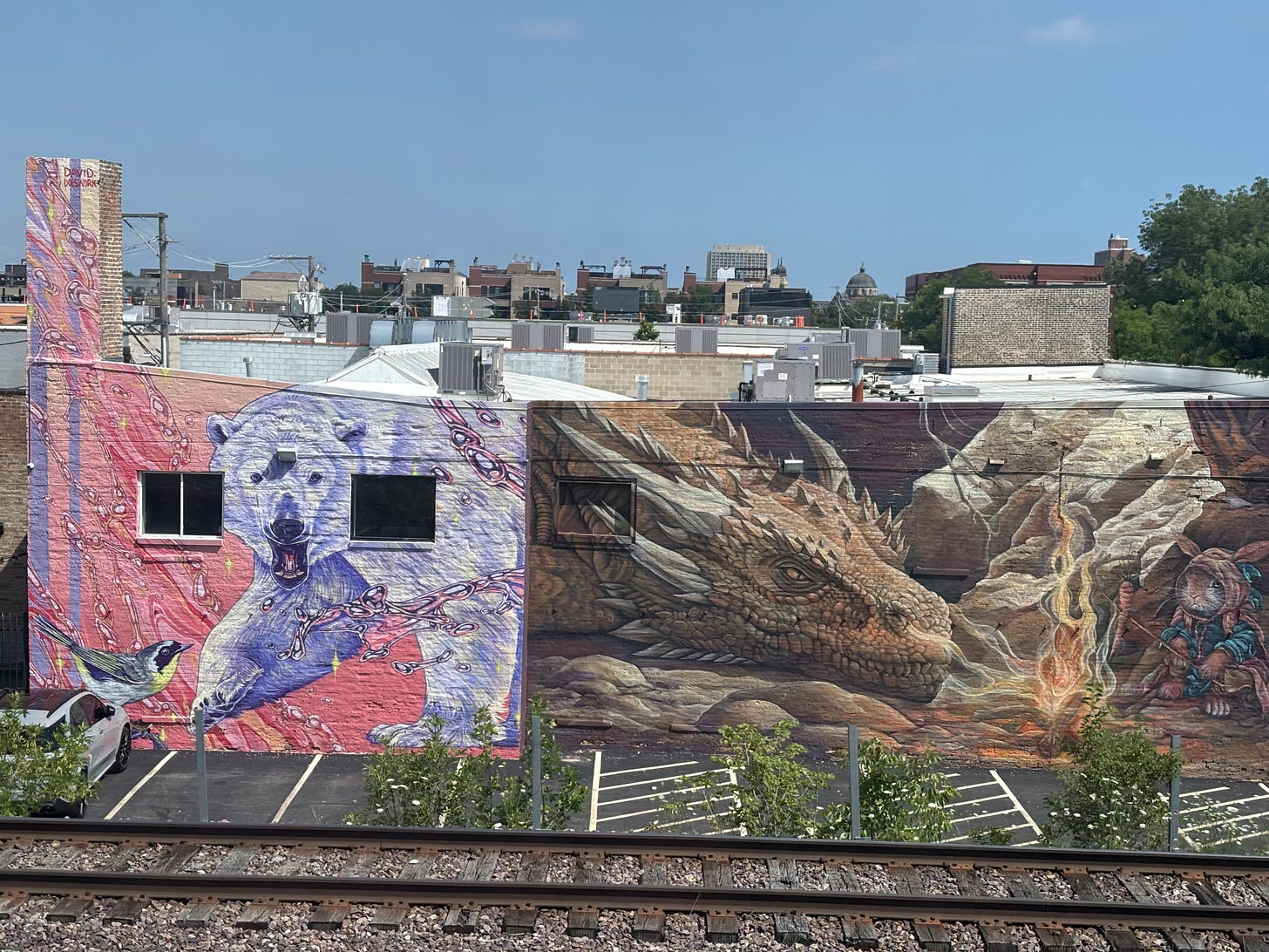 Murals of a polar bear against a pink backdrop and a fire-breathing dinosaur are viewed from a train car