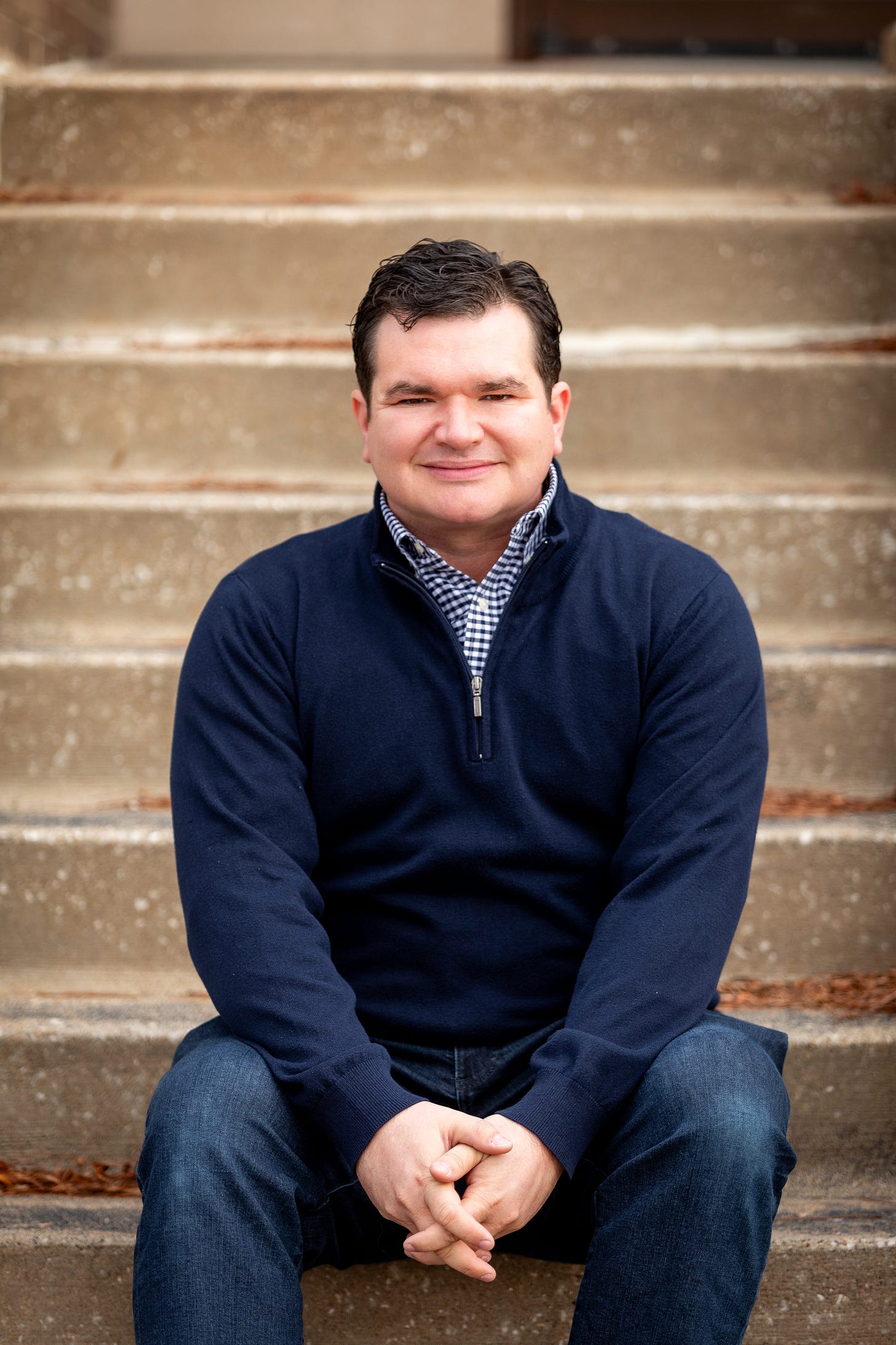 The author, a 30-something white  man dressed in blue business casual, seated on concrete steps