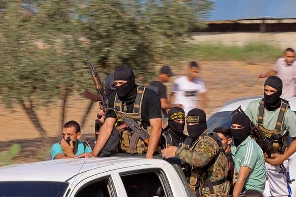 Men with rifles, some dressed in combat gear and wearing black balaclavas, fill the back of a moving pickup.