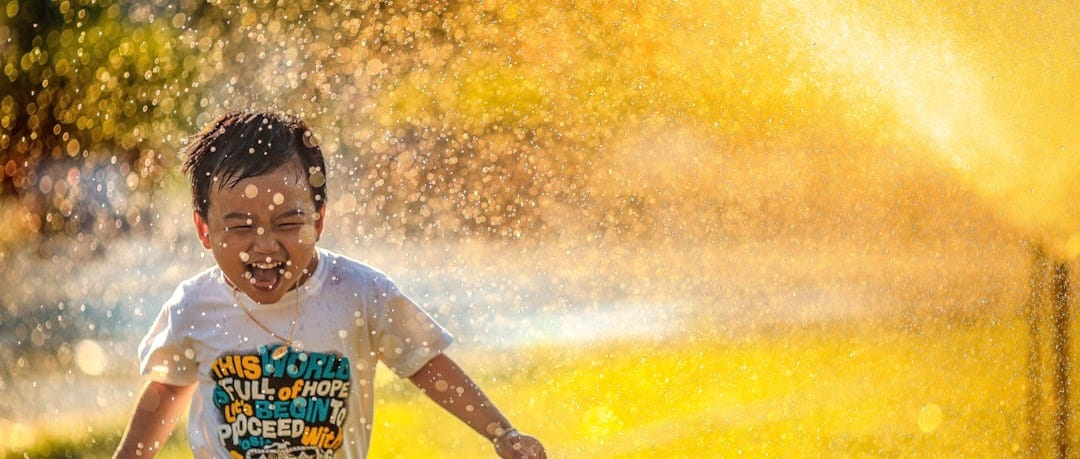 a young boy running through a sprinkle of water