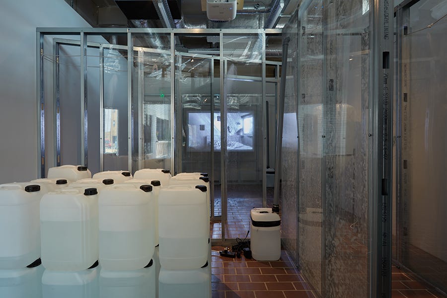 Plastic containers containing water from people’s dehumidifers are stacked in an art gallery. Plastic containers containing water from people’s dehumidifers are stacked in an art gallery.
