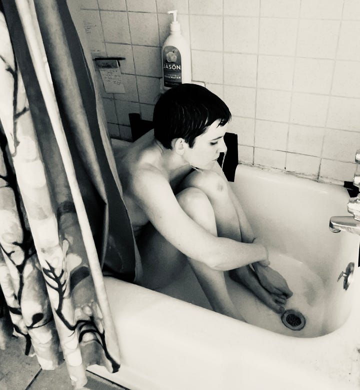 A series of four black and white self-portraits of a person sitting in a bathtub alone. They are covering themself, curled into a ball. The sense is solitary and lonely.
