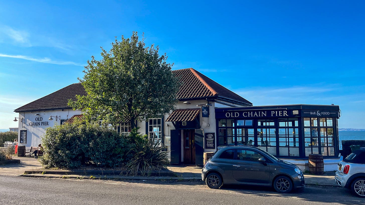 A white pub with an extension to one side. A large tree and bush are located by the entrance.