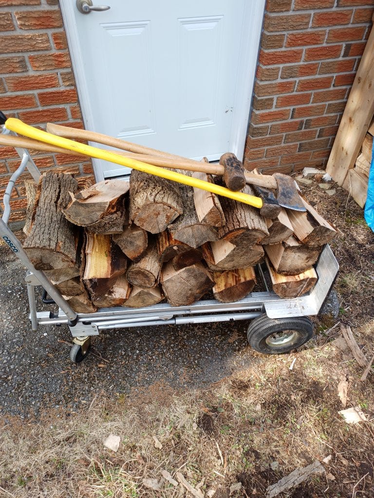 A dolly with some freshly split wood suitable for a fireplace. On top of the wood there's an axe, a splitting axe, and a sledgehammer.