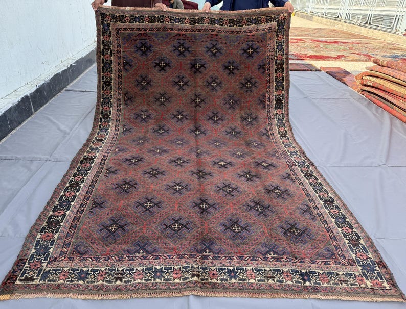 May include: A large rectangular area rug featuring a deep red and dark blue color palette. The central field is covered in a repeating diamond pattern with small cross motifs. The rug is framed by a wide, intricate border with floral elements.