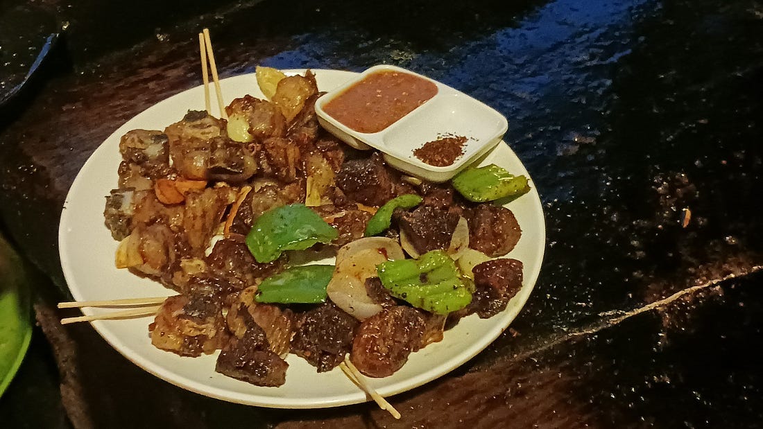 Traditional spicy pork Sekuwa with roasted potatoes on a plate garnished with peppers and onions. A side dish of chilies and sauce sits on the side.