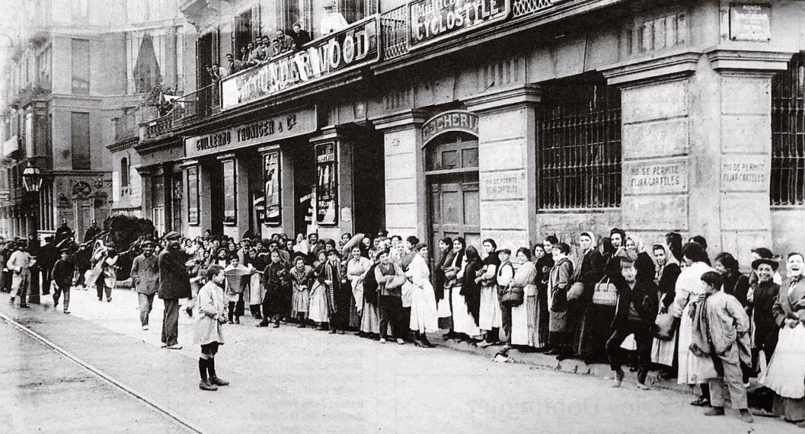 Fotografia storica in bianco e nero che mostra la coda davanti a un negozio che vende carbone a Barcellona. la coda occupa tutto il lato della strada ed è composta da donne e bambini.