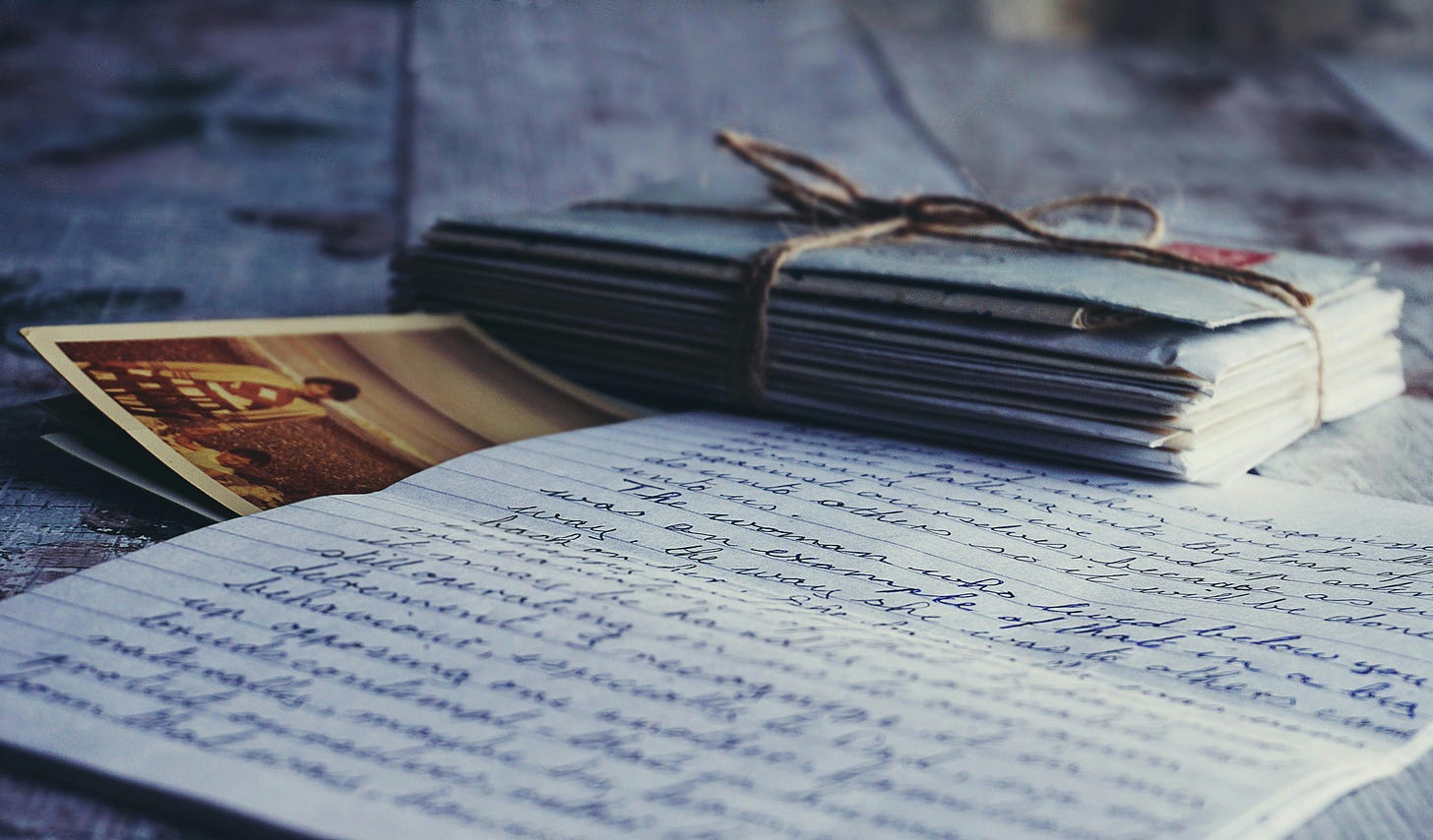 A soft-focus image of a handwritten letter and a stack of envelopes wrapped in twine.