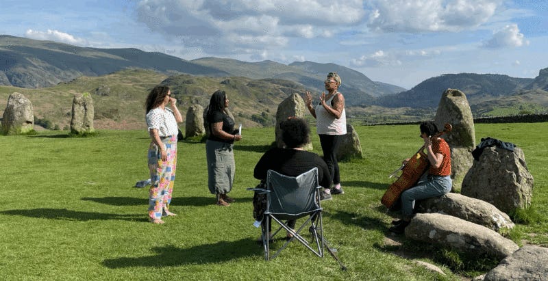 A group of women standing and sat in a group in a large field in the mountains with rocks scattered around the landscape.