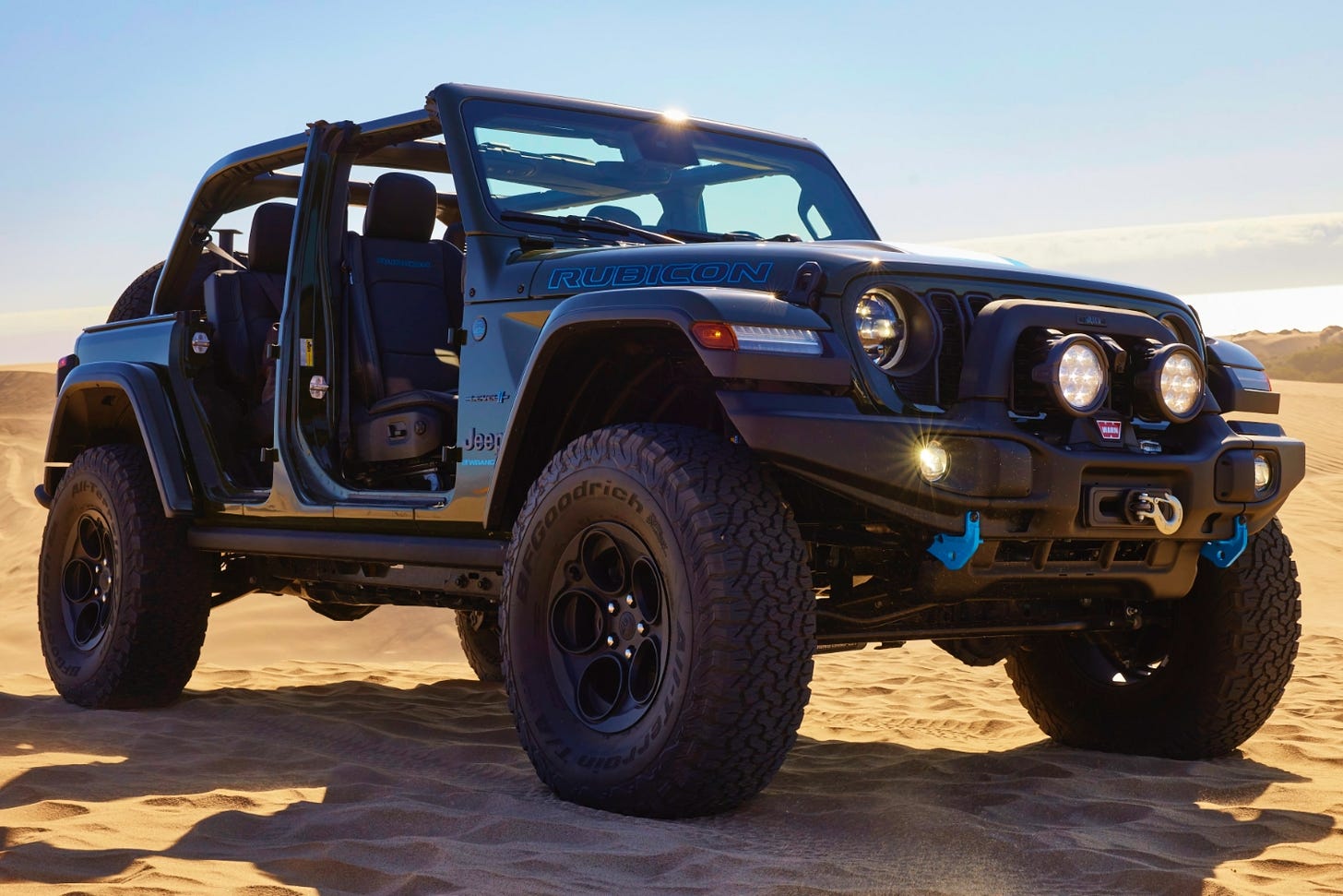 A 2024 Jeep Wrangler Rubicon plug-in hybrid equipped with an AEV off-roading kit is parked on sand in a desert.