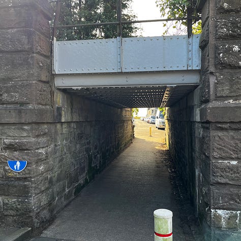 glimpse of a garden beyond a stone archway, the view beneath a low bridge, a grand stone house behind black iron railings