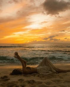 This may contain: a woman laying on top of a sandy beach next to the ocean under a cloudy sky