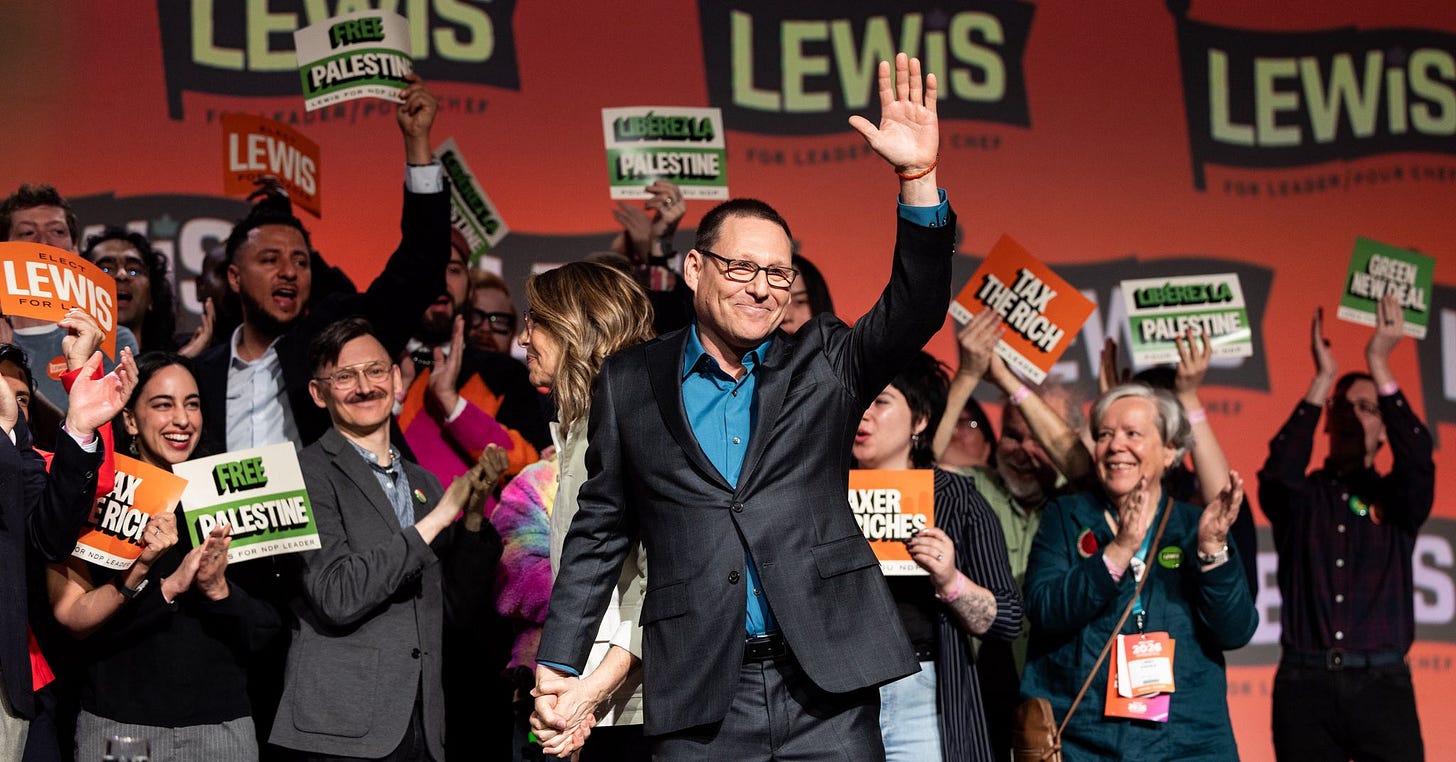 Avi Lewis on stage, waving to the crowd. Behind him are supporters cheering and holding campaign signs.