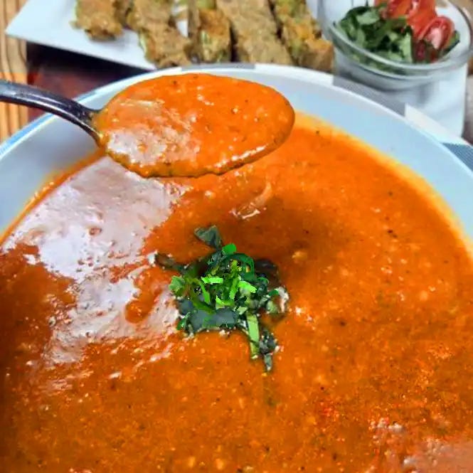 Creamy tomato basil soup in a white bowl with a spoon filled with a mouth full