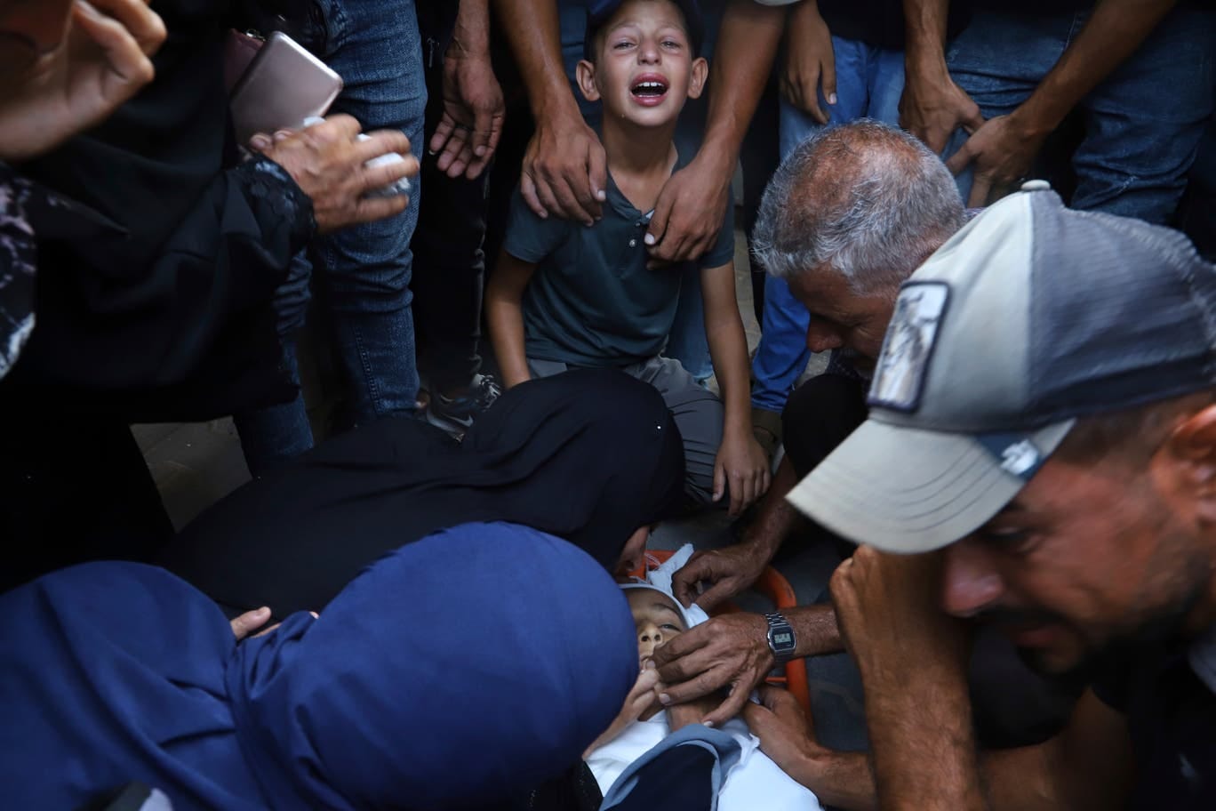 Palestinian relatives mourn over the body of 13-year-old Karim Qdeih, who was killed along with others in overnight Israeli strikes, during his funeral outside Nasser Hospital in Khan Younis, southern Gaza Strip, Saturday, Aug. 23, 2025. (AP Photo/Mariam Dagga)