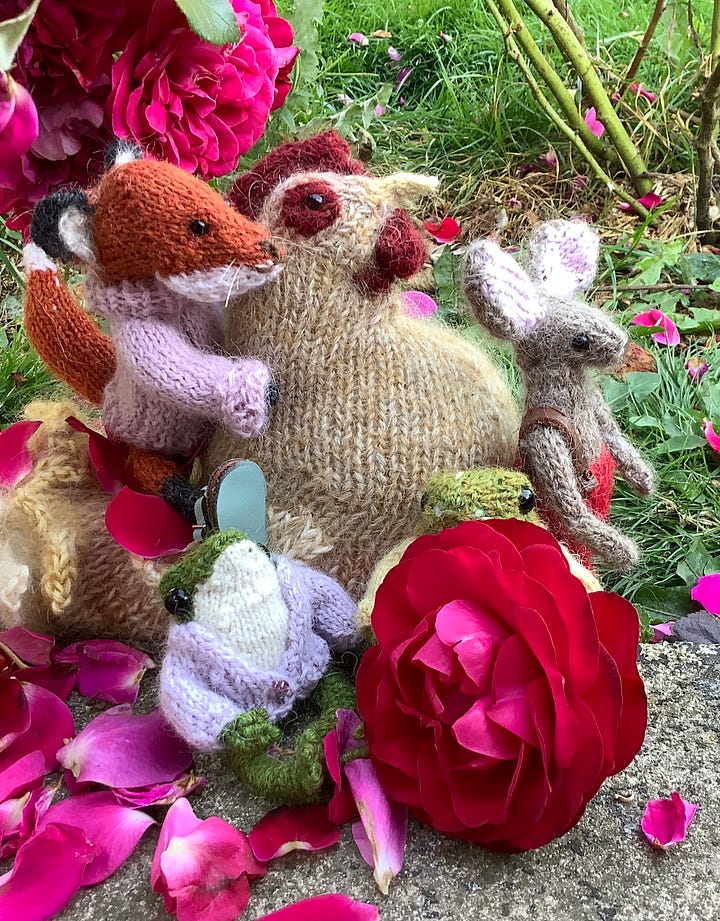 Knitted toys under a red rose bush surrounded by fallen petals
