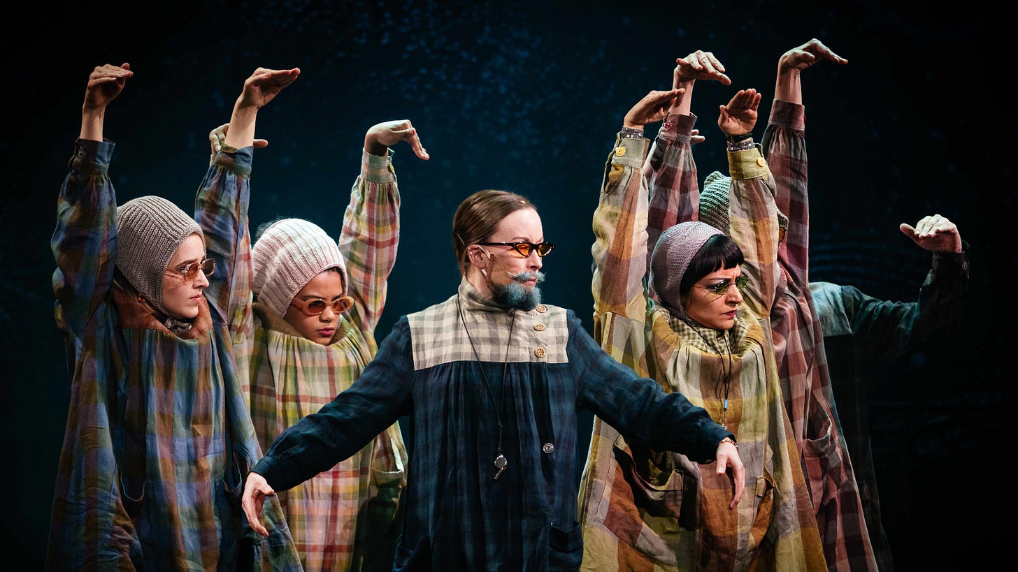 Eccentrically dressed nuns form a chorus line behind a Mother Superior wearing a blue beard.