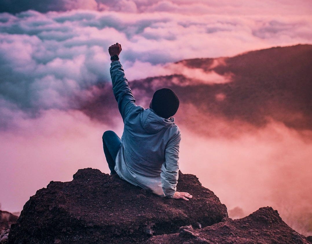 man sitting on mountain cliff facing white clouds rising one hand at golden hour man sitting on mountain cliff facing white clouds rising one hand at golden hour