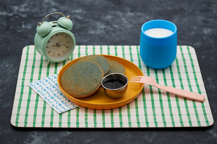 L: Brown tepary beans in wooden bowl; R: Tocabe Blue Corn pancakes on orange plate on green and white checkered placement