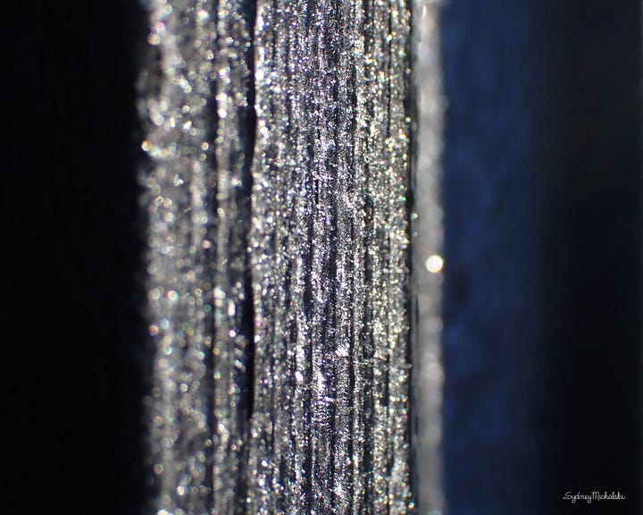 A series of four naturally abstract photographs features vertical stripes of glittering white and golden tones fading into backgrounds of midnight blue and black.