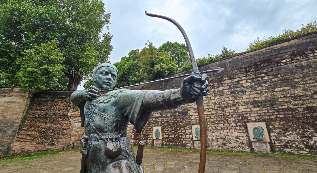 A statue of Robin Hood with a curved brick wall behind it A statue of Robin Hood with a curved brick wall behind it