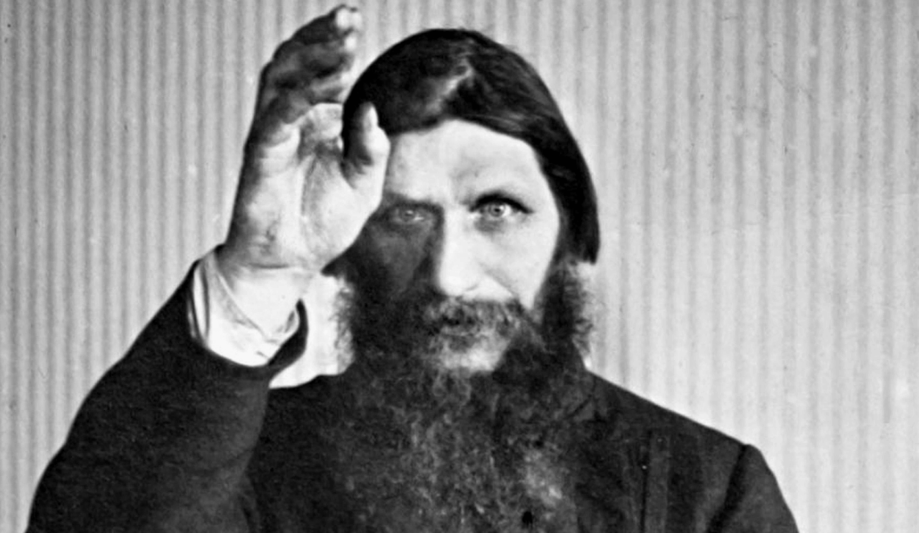 Black and white image of Grigori Yefimovich Rasputin. He is heavily bearded and is raising a hand, looking straight at the viewer. Black and white image of Grigori Yefimovich Rasputin. He is heavily bearded and is raising a hand, looking straight at the viewer.