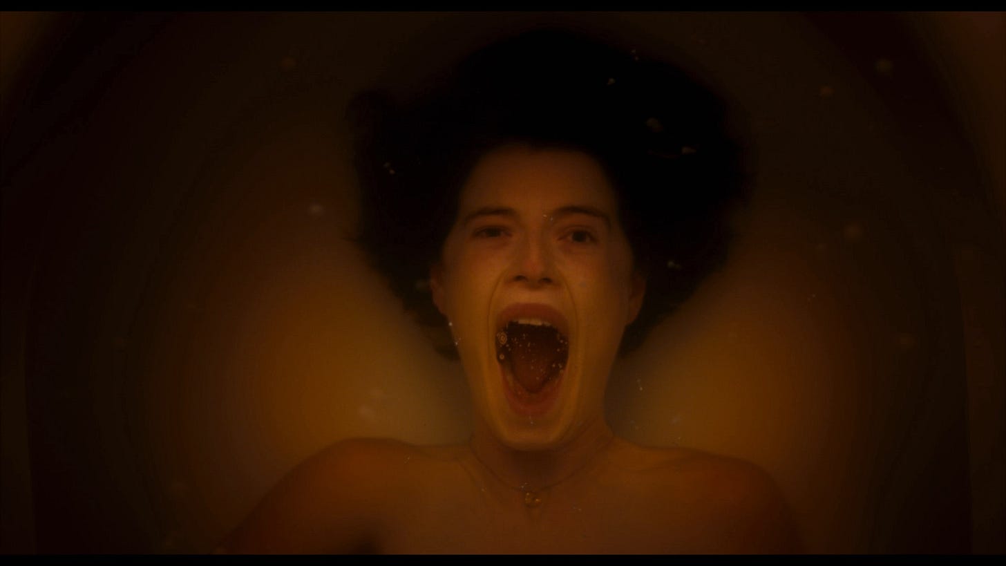 Jessie Buckley as Harper in 'Men,' screaming under water in a bath tub, the water around her a dark orange tint.