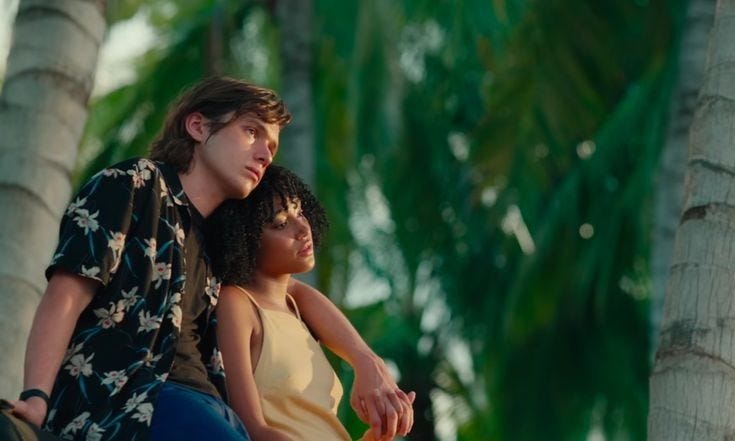 This may contain: two people are sitting on the back of a motorcycle in front of some palm trees
