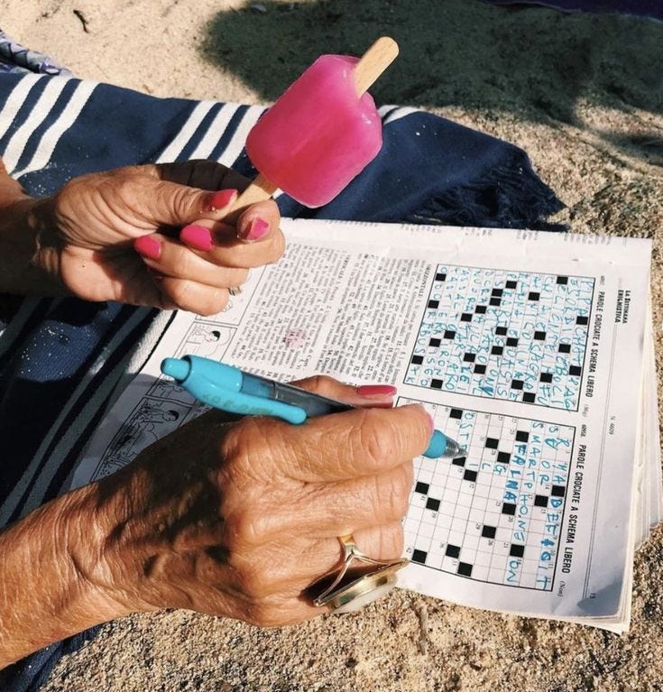 This may contain: an old woman is playing crossword on the beach with her ice cream popsicle