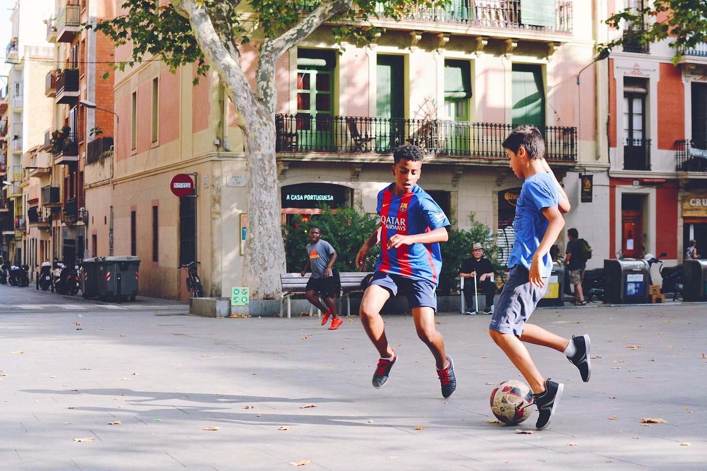 two boy's playing soccer near building during daytime two boy's playing soccer near building during daytime