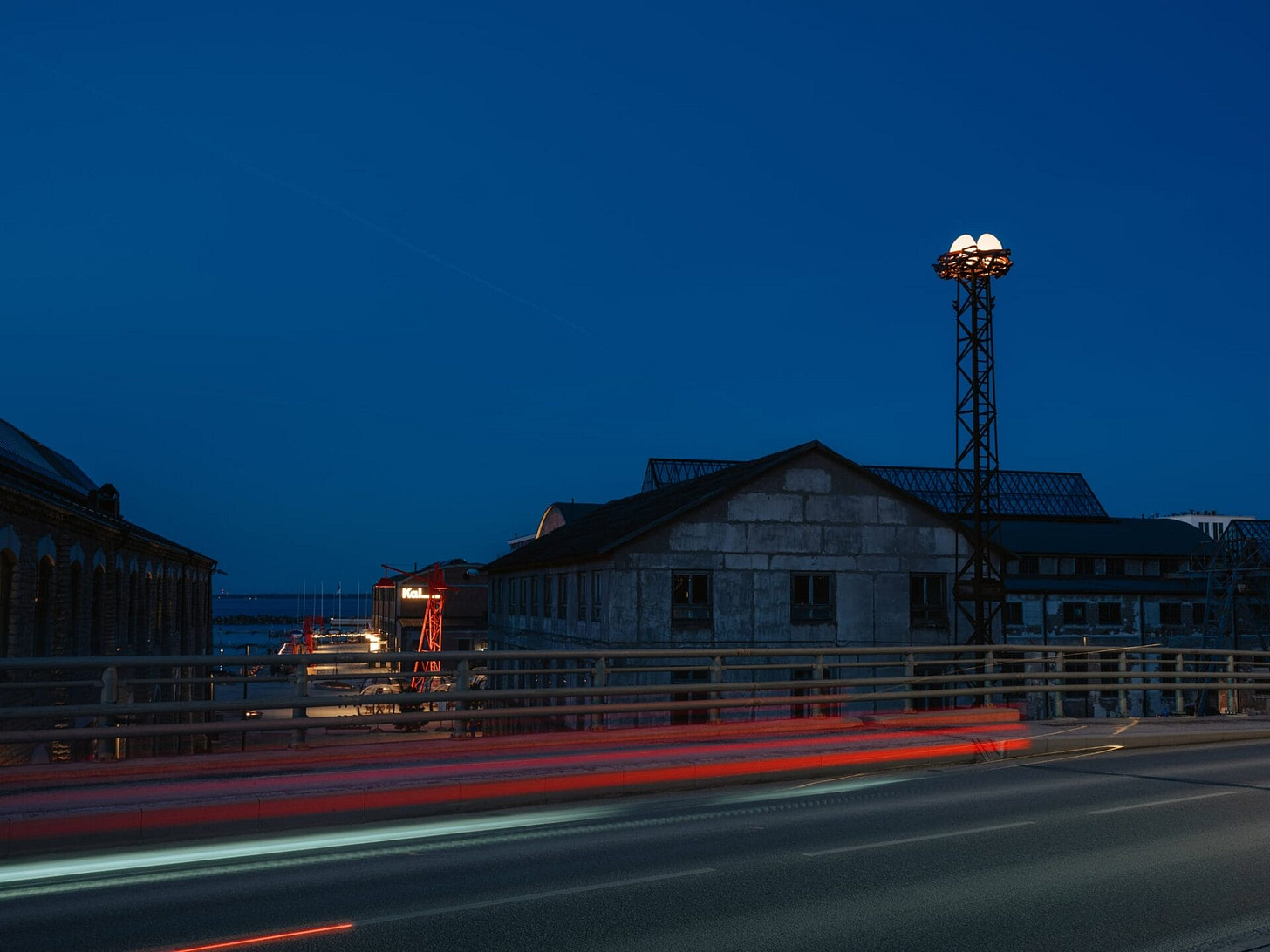 three illuminated eggs perch in a nest atop a tower and glow in the dark next to buildings by the sea