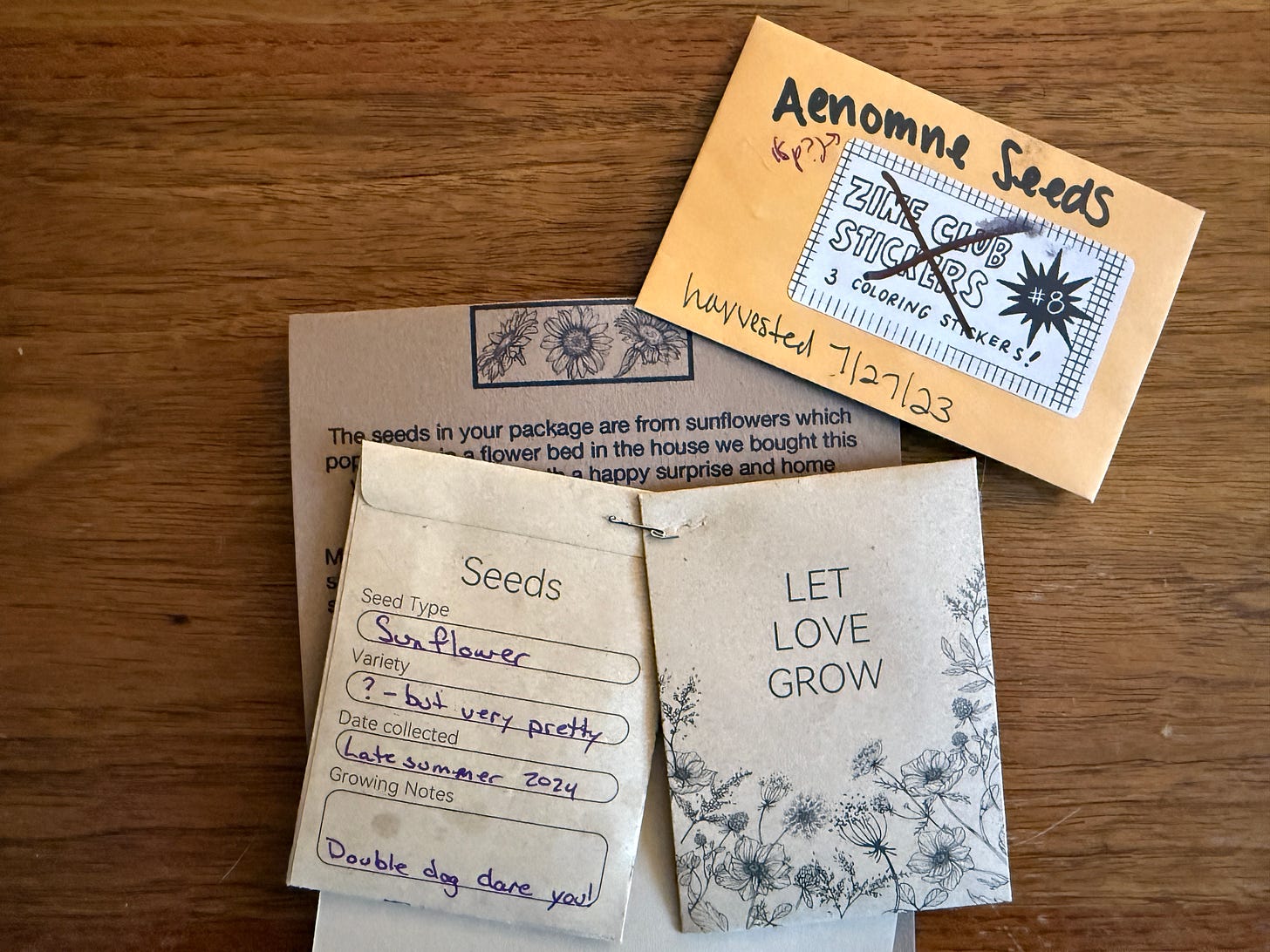 several seed packets labeled with sunflower and anemone seeds. One packet is re-used and features the crossed out text, "Zine stickers" another lists seed type: Sunflower. Variety: ? but very pretty Date COllected: Late summer 2024 Growing Notes: Double dog dare you!