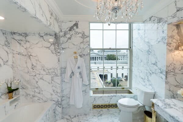The newly renovated Lincoln bathroom in the White House, with marble walls, gold fixtures, a white bath robe and a window with a view of the White House.