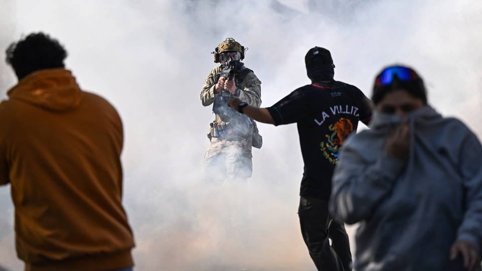 ICE Agent in a cloud of tear gas aiming a weapon at unarmed protestors in Chicago