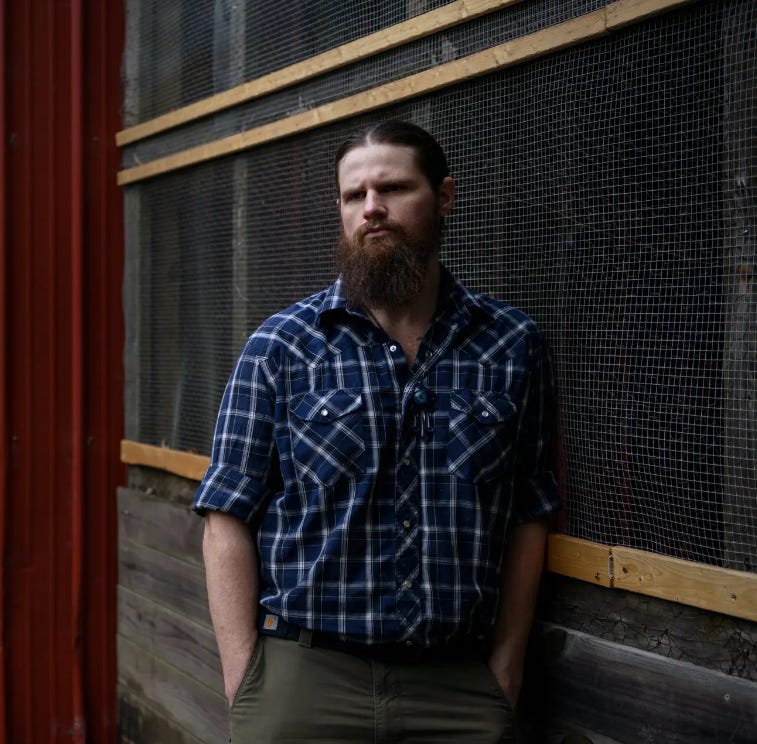 Army veteran Derrick Wynne, bearded and in a plaid shirt, leaning against a wooden wall Army veteran Derrick Wynne, bearded and in a plaid shirt, leaning against a wooden wall