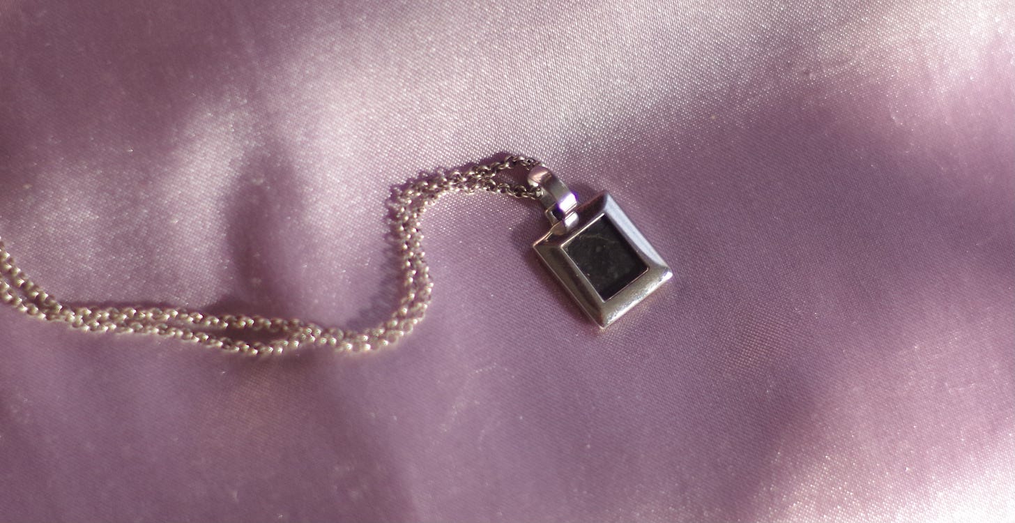 A white gold pendant, with a dark stone center made of moon rock, resting on a background of pink fabric