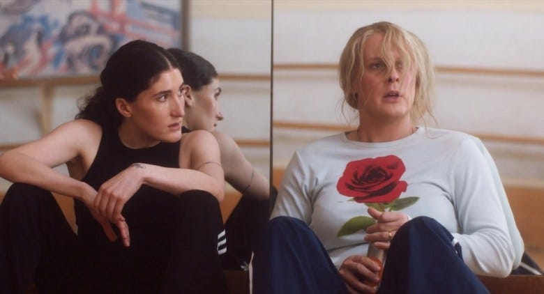 In a still from "Maddie's Secret," actor Kate Berlant sits wearing all black, looking to her left at actor John Early dressed as the main character Maddie. In a still from "Maddie's Secret," actor Kate Berlant sits wearing all black, looking to her left at actor John Early dressed as the main character Maddie.