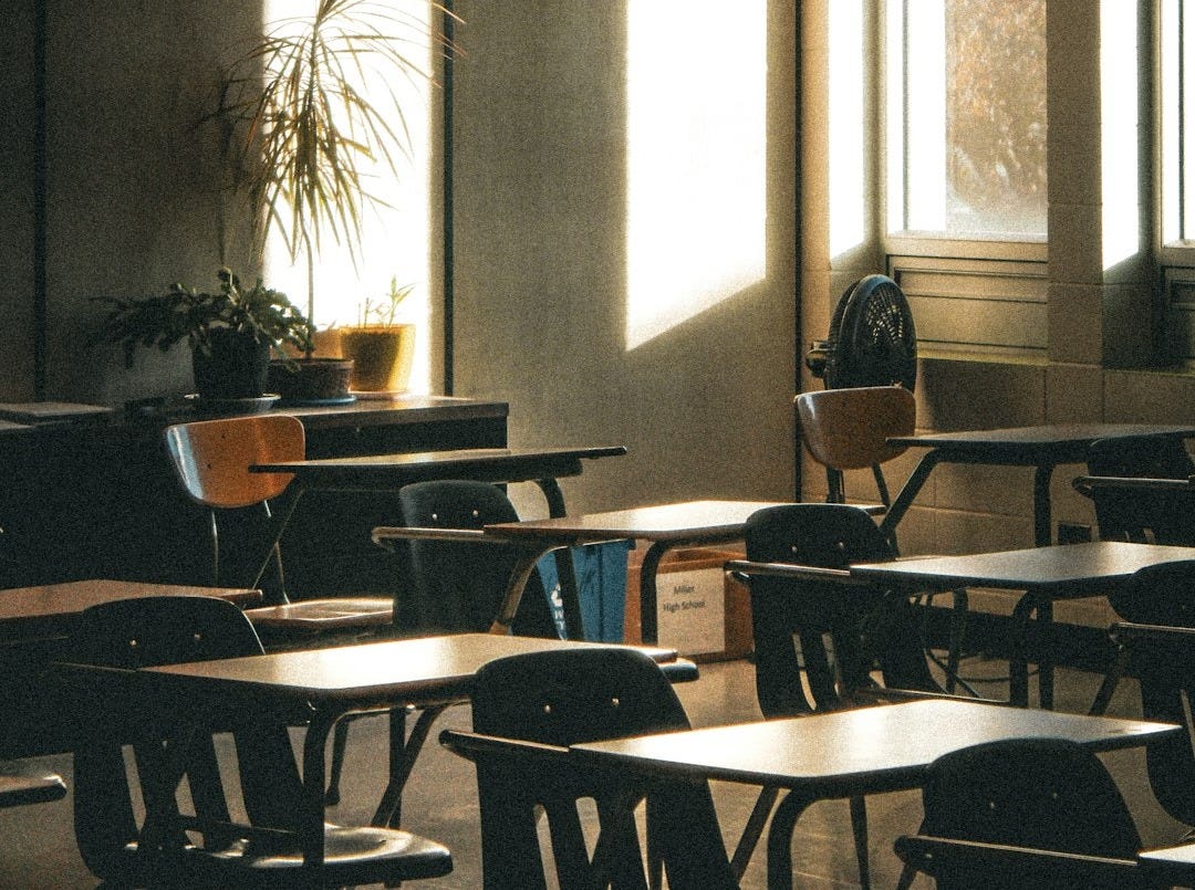 Sunlight streams into an empty classroom with desks.