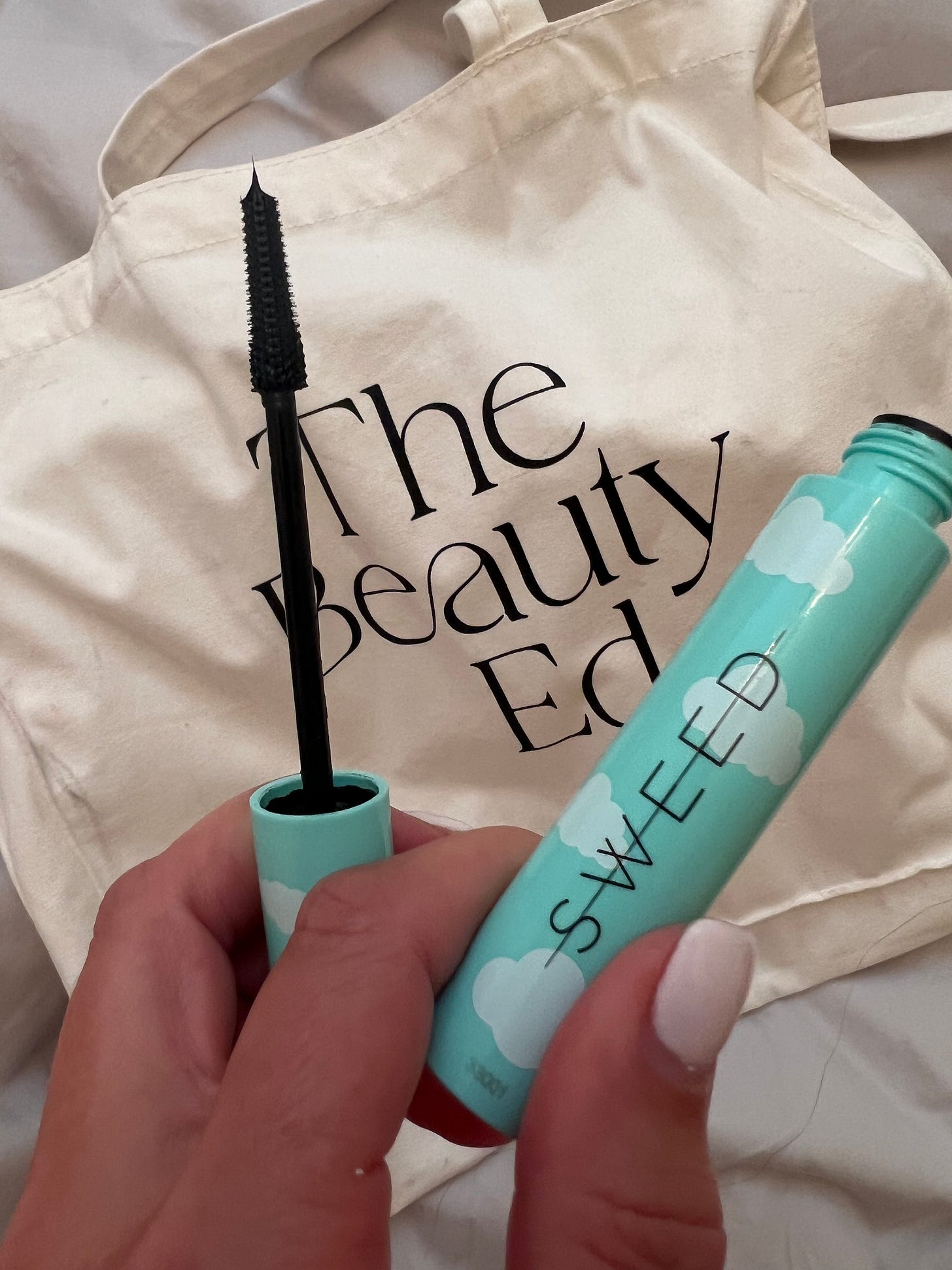 A tube of Sweed The Cloud Mascara in front of a The Beauty Ed® tote bag A tube of Sweed The Cloud Mascara in front of a The Beauty Ed® tote bag