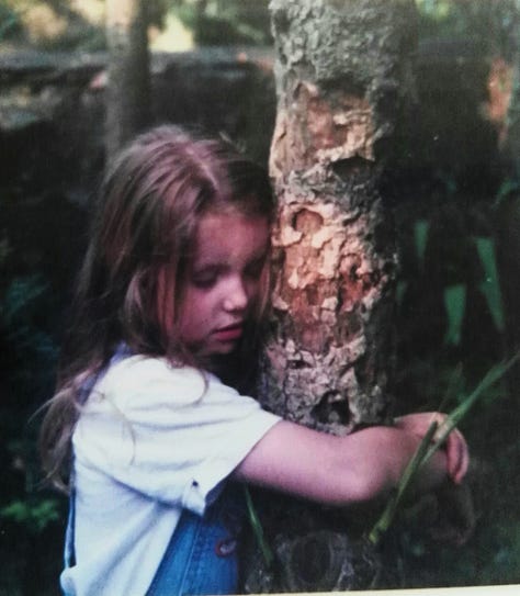 A young child and a woman hugs a tree.