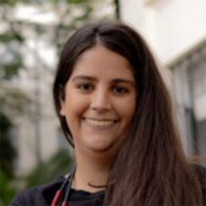 Mulher de camiseta preta e colar comprido vermelho e preto. Tem cabelos compridos escuros e sorri para a foto Mulher de camiseta preta e colar comprido vermelho e preto. Tem cabelos compridos escuros e sorri para a foto