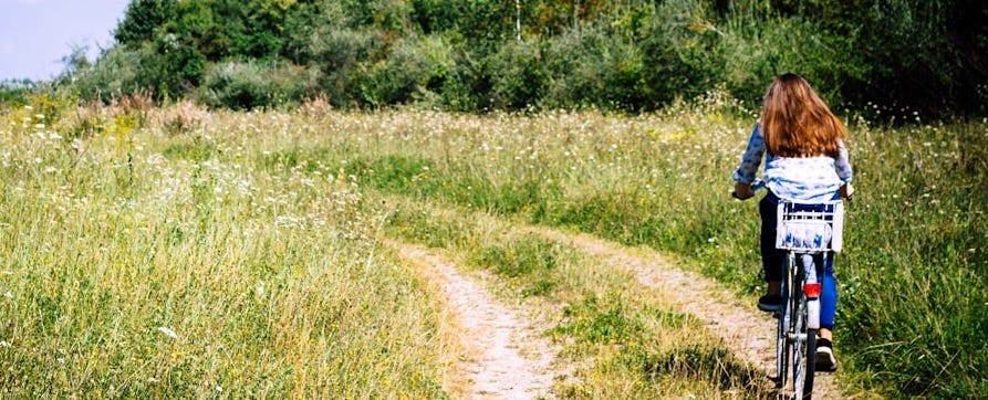 woman biking between grasses