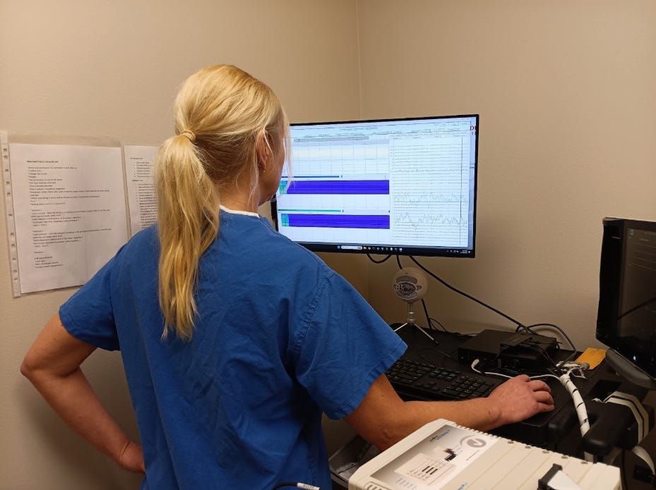 A person in blue scrubs analyzes data on a computer monitor in a medical setting.
