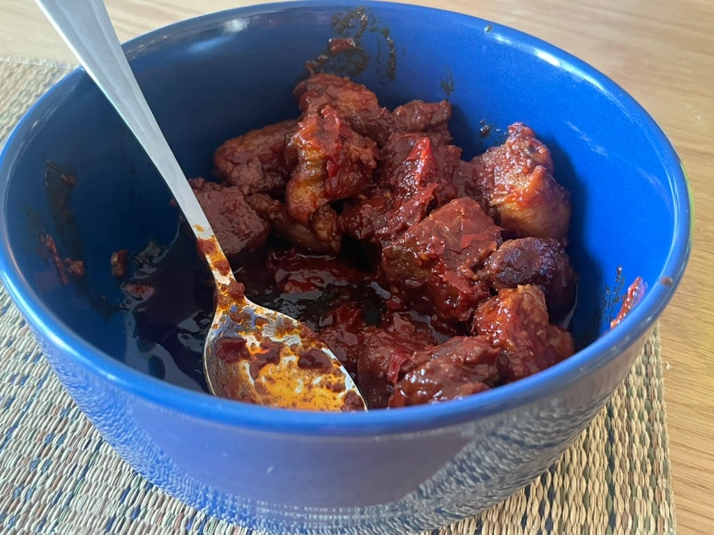 A blue bowl containing chunks of meat that is covered in a red sauce