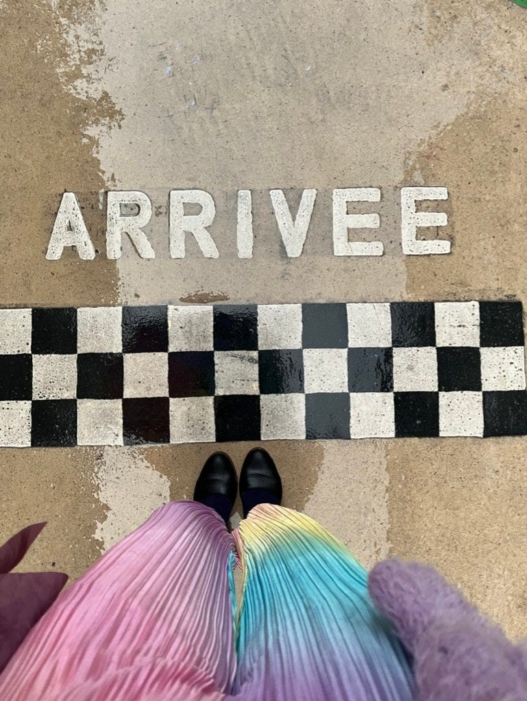 A picture of my Patina black heeled mary janes with my feet about to pass a finish line and the word ARRIVEE written above it