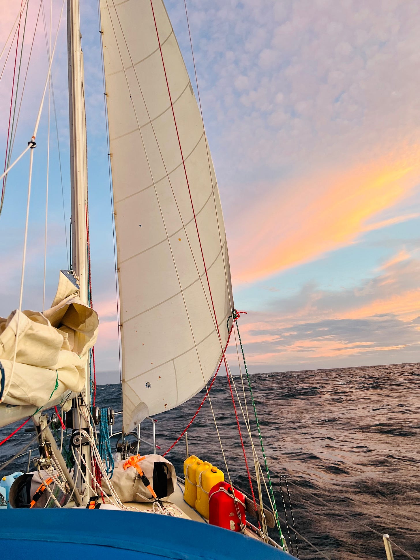 Sunset behind headsail on open ocean