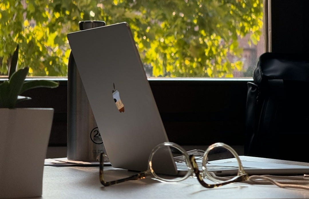 Laptop and glasses on desk with window view.