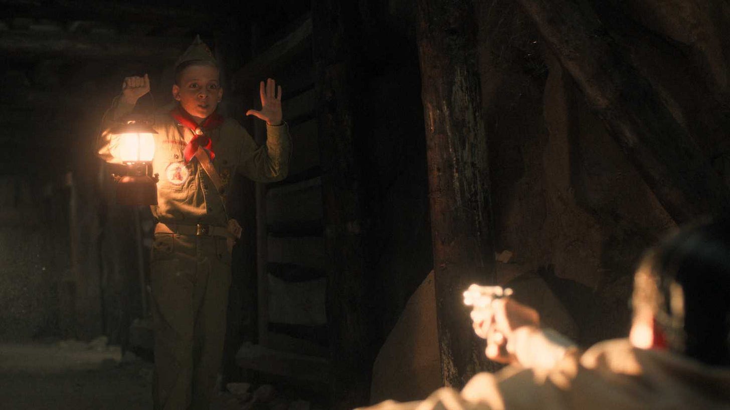 A young Henry Creel (Maksim Blatt) holds his hands up as a man a mineshaft in Nevada points a gun at him in Stranger Things season 5, episode 6